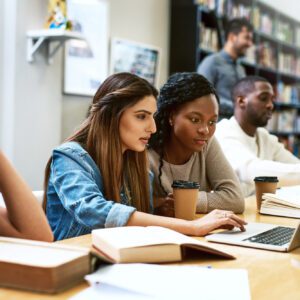 A group of people sitting at tables with books and laptops.