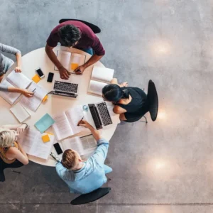 A group of people sitting around a table with laptops.