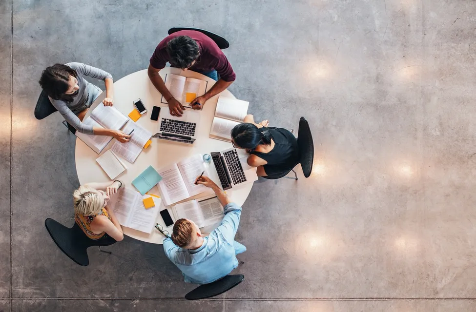 A group of people sitting around a table with laptops.