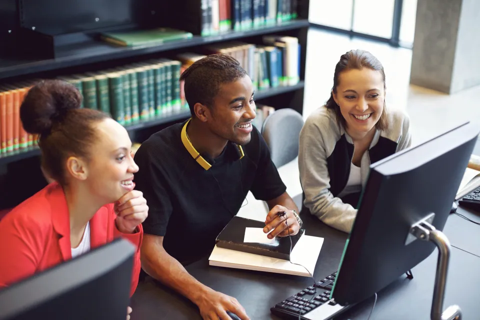 Three people sitting at a table with computers.