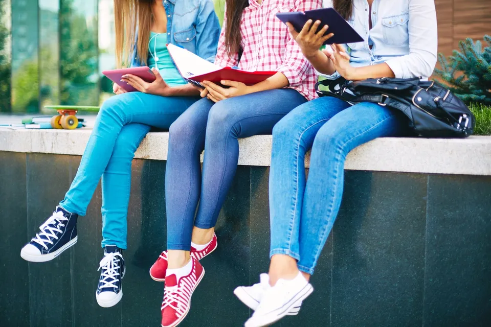 A group of girls sitting on top of a wall reading books.